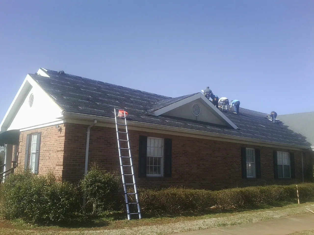Crew tearing shingles off a brick ranch roof with a ladder set — Metal Roof Repair work by our crew in Sidney Center