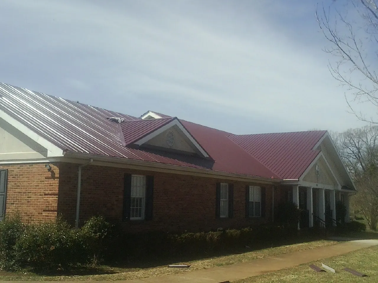 Red metal roof with gabled entries on a long brick building, from a Hail Damage Roof Repair job in Sidney Center