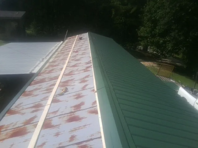 Old rusted panels beside newly installed green metal roofing — Wind Damage Roof Repair by Roofing Brothers in Sidney Center