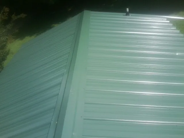 New green metal panels meeting at the ridge of a roof — Flat Roof Repair work by our crew in Sidney Center