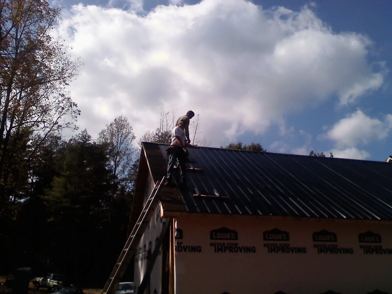 Roofer fastening dark metal panels high against a cloudy sky in Sidney Center