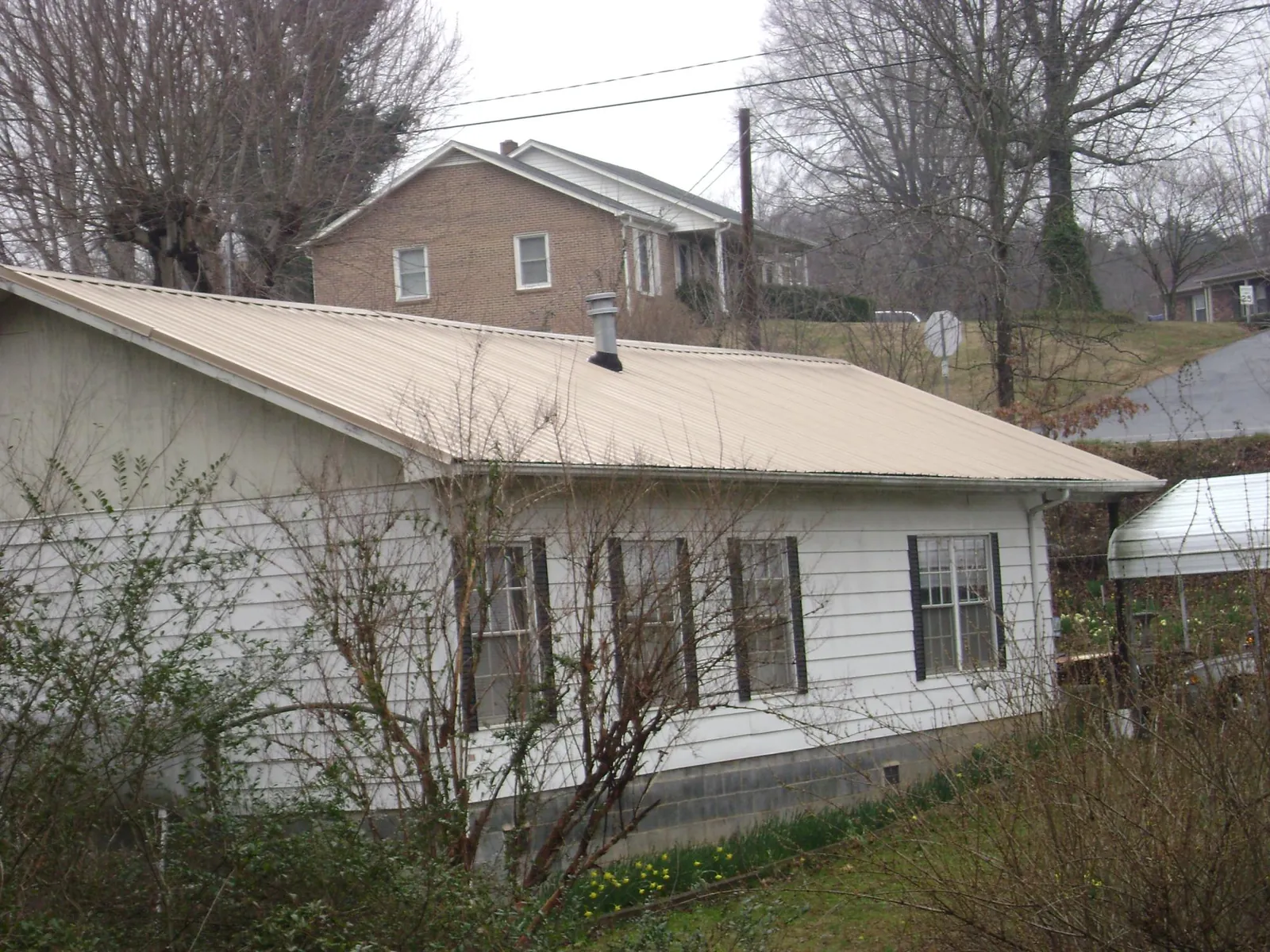 Tan metal roof on a white sided house set into a hillside — Commercial Roofing by Roofing Brothers in Sidney Center