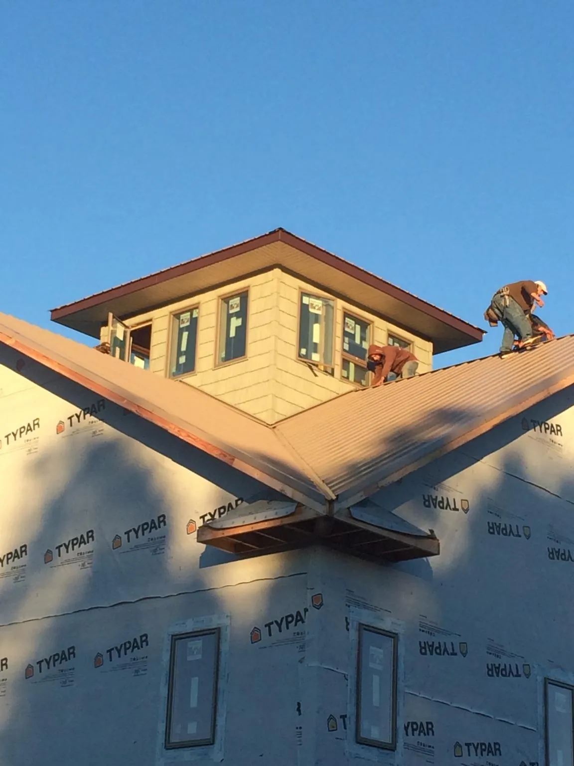 Roofers working around a rooftop cupola on a new metal roof at sunset — Roof Waterproofing in Sidney Center by Roofing Brothers
